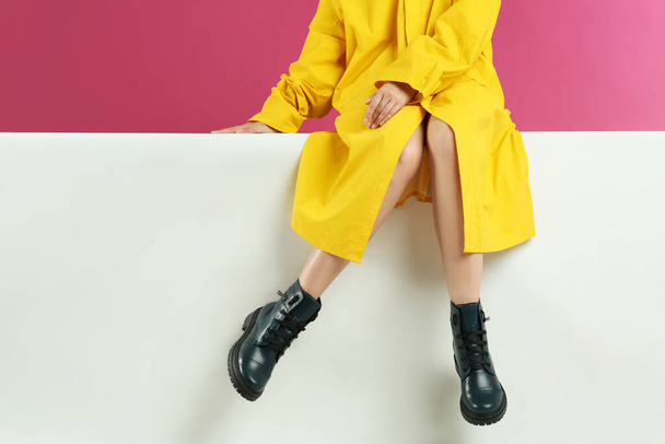 Woman in stylish boots sitting on color background, closeup - Фото, зображення