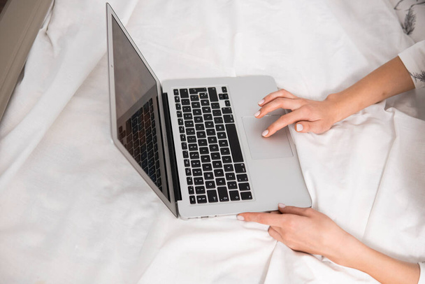 Top view of a woman sitting on a bed , using laptop. Working at home concept. Girl is working on her laptop in bed with white linens. Relaxing working process. Stay at home. - Foto, Imagem