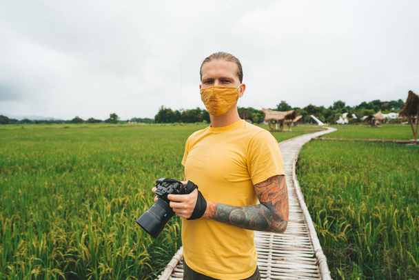 Man photographer in yellow t-shirt is walking at bamboo bridge in rice field - Foto, afbeelding