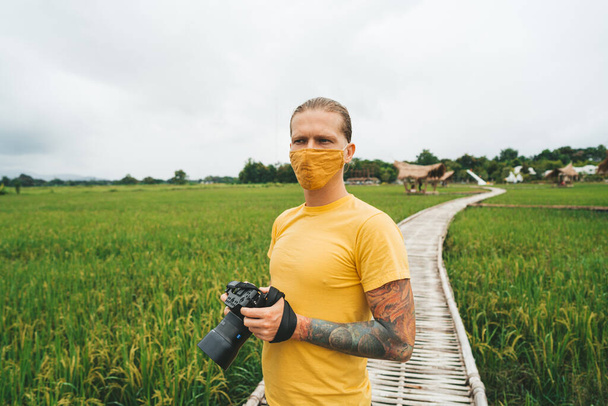Man photographer in yellow t-shirt is walking at bamboo bridge in rice field - Foto, afbeelding