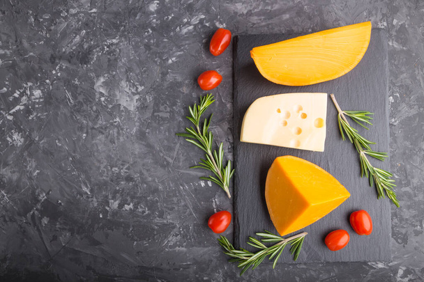 Vari tipi di formaggio con rosmarino e pomodori su lavagna nera su fondo di cemento nero. Vista dall'alto, disposizione piatta, spazio di copia. - Foto, immagini
