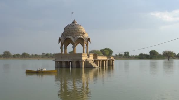 Gele steen gemaakte structuren te midden van het water lichaam, Gadisar meer in de prachtige stad Jaisalmer, werd kunstmatig gebouwd voor het behoud van water. Schoot op Jaisalmer, Rajasthan, India. Blauwe lucht achtergrond. - Video
