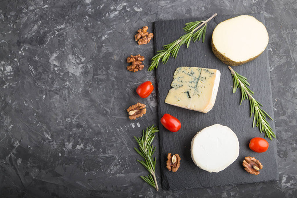White goat cheese and various types of cheese with rosemary and tomatoes on black slate board on a black concrete background. Top view, copy space, flat lay. - Foto, Imagen