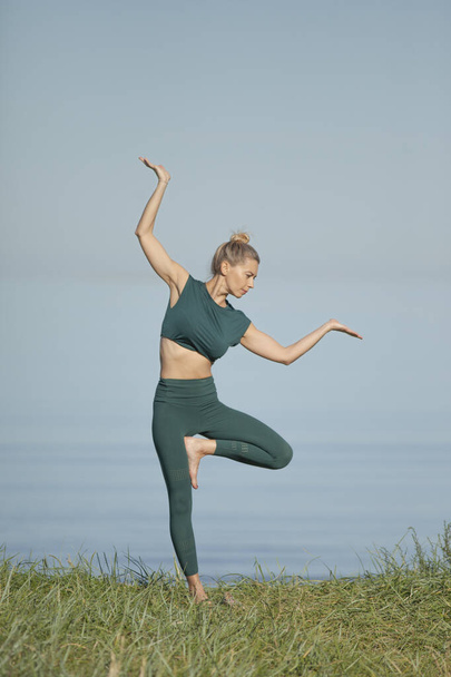 Yoga-Frau in grüner Sportbekleidung entspannt am Meer - Foto, Bild
