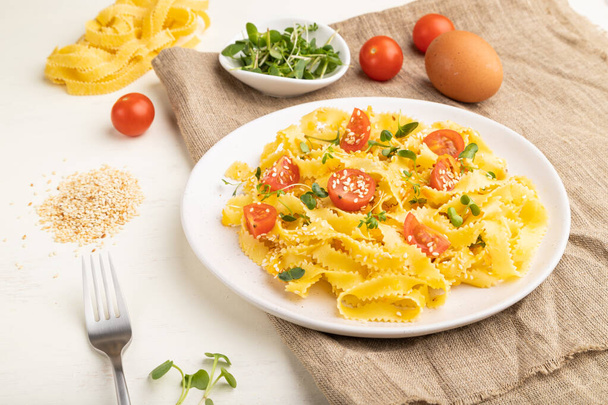 Reginelle semolina pasta with tomato, eggs, sesame and microgreen sprouts on a white wooden background and linen textile. Side view, close up. - Φωτογραφία, εικόνα