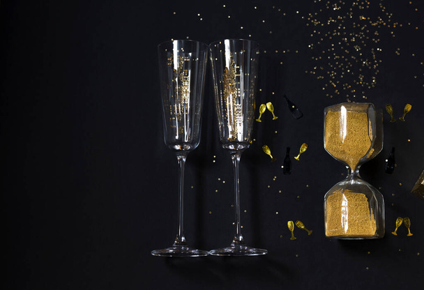 Gold christmas flat layout with confetti, two champagne glasses and hourglass on black background. New Year festive concept. Top view. Copy space - Valokuva, kuva