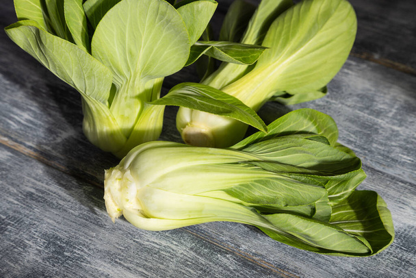 Fresh green bok choy or pac choi chinese cabbage on a gray wooden background. Hard light, contrast. Side view, close up. - Foto, Imagem