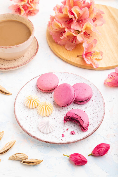 Macarons viola o torte di amaretti con tazza di caffè su uno sfondo di cemento bianco decorato con fiori. Vista laterale, da vicino. - Foto, immagini