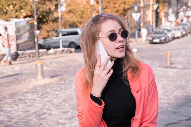 Młoda stylowa kobieta w okularach przeciwsłonecznych rozmawiająca przez telefon komórkowy w środku miasta - Zdjęcie, obraz