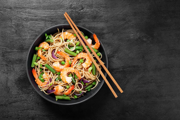 Stir fry noodles with shrimps and vegetables in black bowl. - Photo, Image