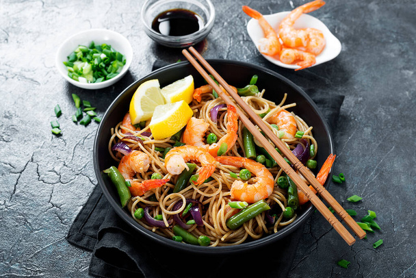 Stir fry noodles with shrimps and vegetables in black bowl. - Photo, image