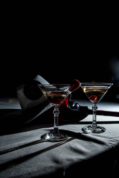 A couple of martini glasses with cherry and a cowboy hat on dark background - Фото, зображення
