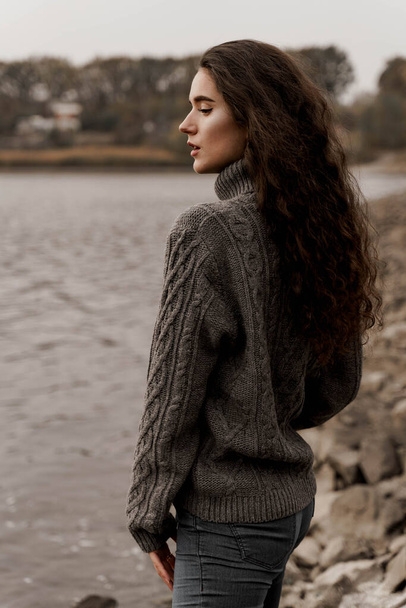Girl with curly hair on the background of birch with stones and lake in autumn - Foto, afbeelding