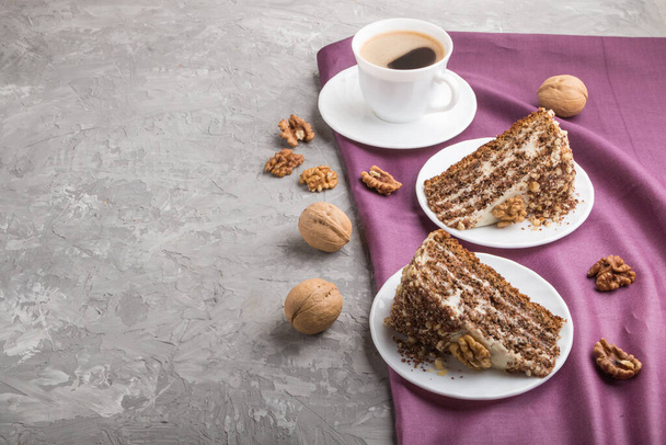 Homemade cake with milk cream and walnuts with cup of coffee on a gray concrete background and purple textile. side view, copy space. - Photo, Image
