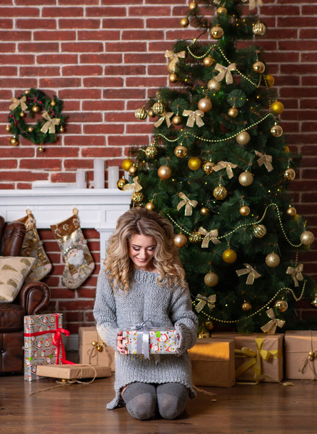 Beautiful young woman sitting near decorated Christmas tree. Christmas, New Year and winter holidays concept. - Zdjęcie, obraz