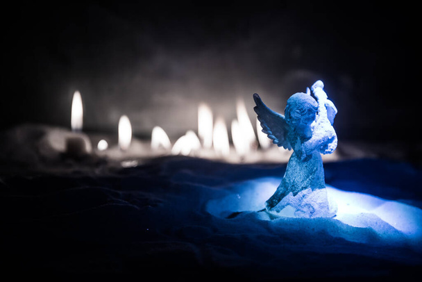 Χριστουγεννιάτικος άγγελος στέκεται στο χιόνι με πολλά κεριά στο παρασκήνιο. Μικρός λευκός φύλακας άγγελος στο χιόνι. Εορταστικό φόντο. Χριστούγεννα και Πρωτοχρονιά έννοια. Επιλεκτική εστίαση - Φωτογραφία, εικόνα