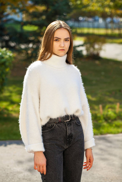Young girl in a woolen sweater and black jeans posing in an autumn park - Foto, Bild