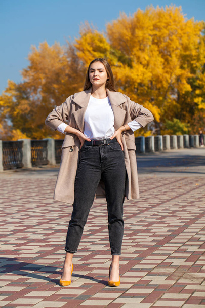 Full body portrait of a young beautiful brunette girl in beige coat and black jeans - Fotó, kép
