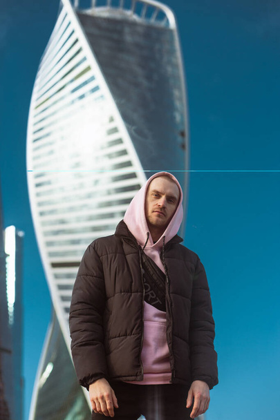 Handsome casual man in black jacket and pink hoody standing on a skyscraper view - 写真・画像
