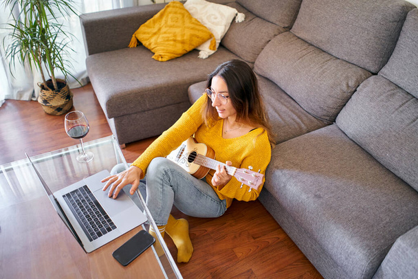 Vista superior de la mujer tomando lecciones ukelele en línea de su computadora portátil durante cuarentena covid. - Foto, imagen
