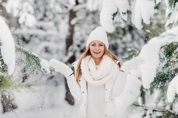 Portrait of a woman in white clothes in a cold winter forest. A girl with a white hat on her head in a snow-covered winter forest. - Zdjęcie, obraz