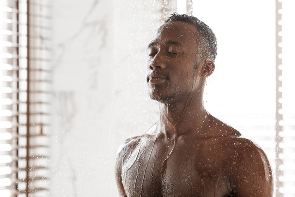 Houkutteleva musta kaveri ottaa virkistävä suihku aamulla sisätiloissa - Valokuva, kuva