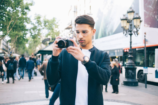 Fiatal férfi fotós alkalmi ruhák és karóra áll a zajos város utcáján, és fotózás a fényképezőgép nappal - Fotó, kép
