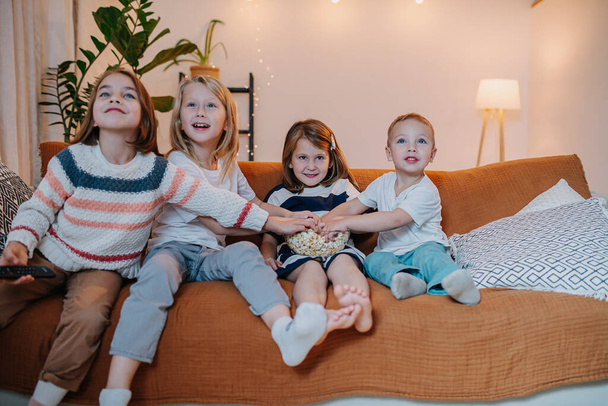 Keen entertained children from 5 to ten years old sitting on a couch, watching television, eating popcorn. They are very keen and jumpy. - Fotoğraf, Görsel