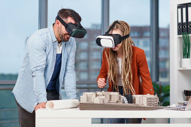 Couple of architects or engineers at VR goggles working with mock-up of future residential area in modern office. - 写真・画像