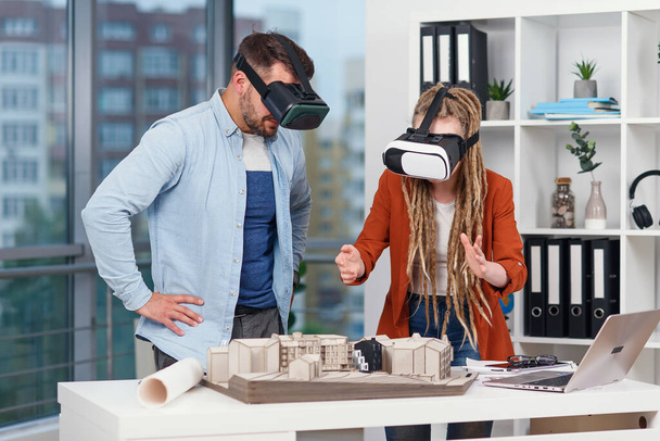 Couple of architects or engineers at VR goggles working with mock-up of future residential area in modern office. - Φωτογραφία, εικόνα
