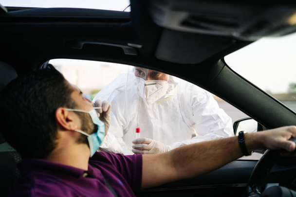 Doctor doing a PCR test COVID-19 on a patient through the car window. PCR diagnostic for Coronavirus presence,doctor in PPE holding test kit - Fotografie, Obrázek