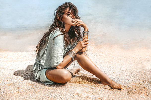 Beautiful young stylish woman sitting on sand on the beach - Fotoğraf, Görsel