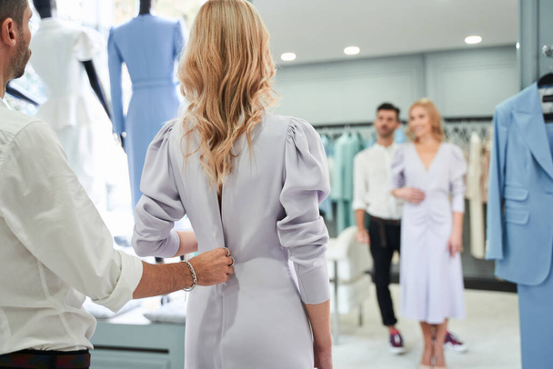 Woman looking at the mirror while stylist buttoning the dress - Photo, image