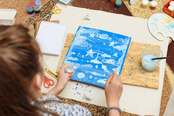 girl draws at home, artistic creation, makes creative artwork from paper, paints and brushes - 写真・画像
