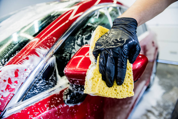 Työntekijä pesee punaista autoa sienellä autopesussa - Valokuva, kuva