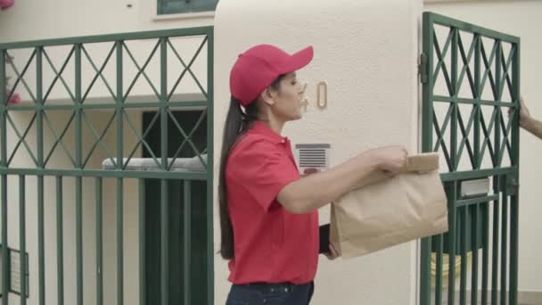 宅配便の女の子がドアベルを鳴らし、顧客にパッケージを与える - 映像、動画