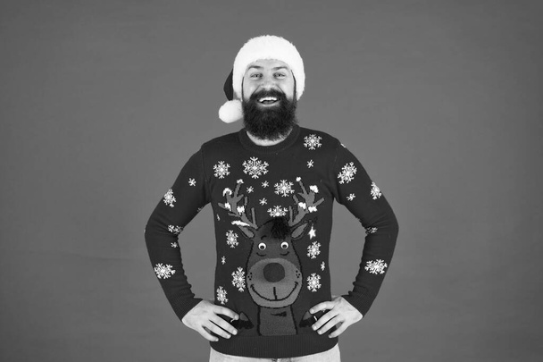 Happy new year. Join holiday party. Winter party outfit. Invitation ugly sweaters party. Sweater with deer. Hipster bearded man wear winter sweater and hat red background. Holly jolly christmas - Fotografie, Obrázek