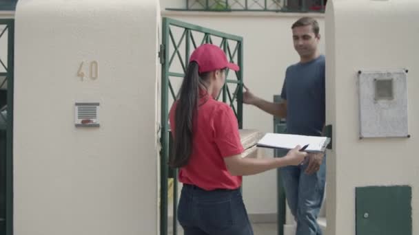 Female courier in red cap delivering package to customers door - Footage, Video