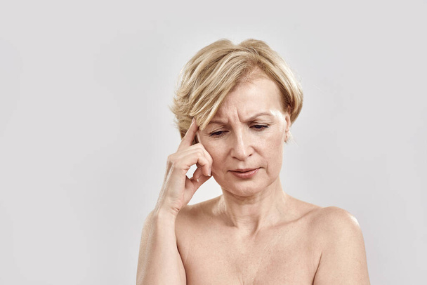 Portrait of beautiful blonde middle aged woman with puzzled expression, thinking deeply about something, posing isolated against grey background. Body language and face expression concept - Fotó, kép
