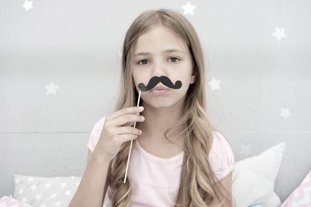 Pajamas party concept. Girl fake mustache at pajamas party. Cheerful kid posing mustache. Photo booth props ideas. Printable accessories for party. Girl long blonde hair posing with photo booth props - Foto, immagini