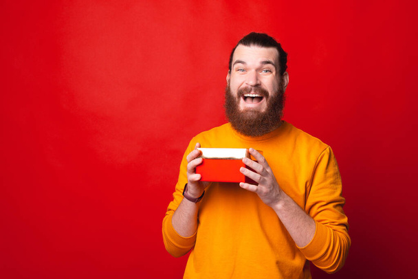 Een man die erg enthousiast is over zijn gave die hij bij een rode muur vasthoudt. - Foto, afbeelding