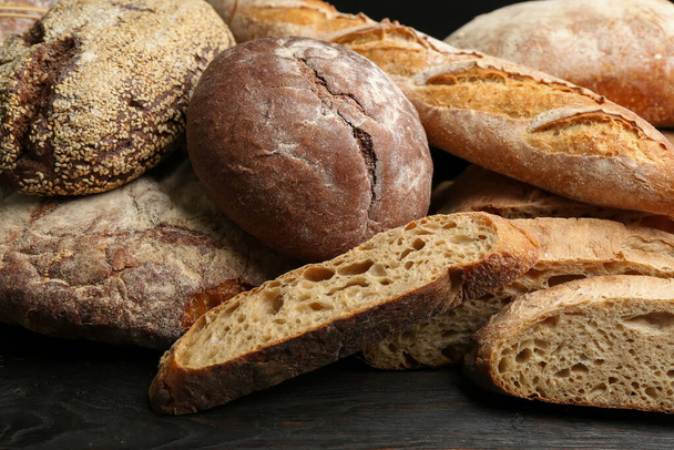 Different kinds of fresh bread on black wooden table, closeup - Фото, изображение