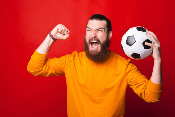 A bearded man is holding a soccer ball and is screaming of excitement - Фото, изображение