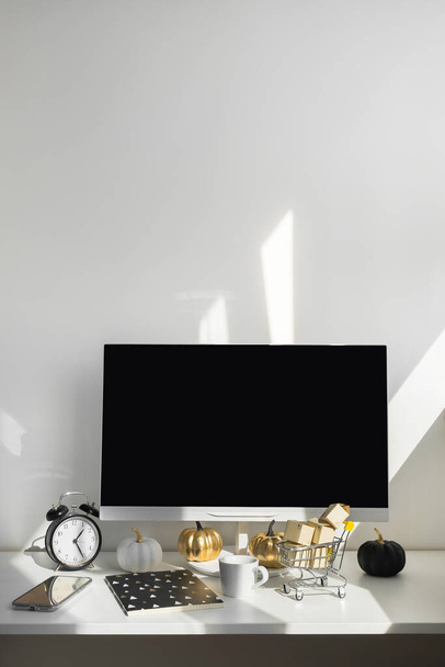Üres képernyős asztali számítógép a modern minimális irodai szobában, őszi dekorációval. Papírdobozok egy szekéren az asztalon. Online vásárlási koncepció - Fotó, kép