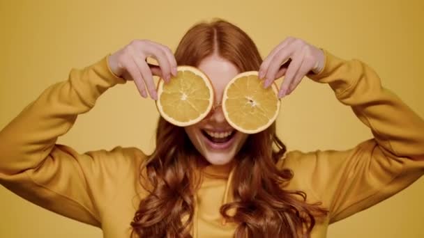 Linda chica sosteniendo rodajas de naranja en el estudio. Mujer mostrando lengua y guiño - Metraje, vídeo