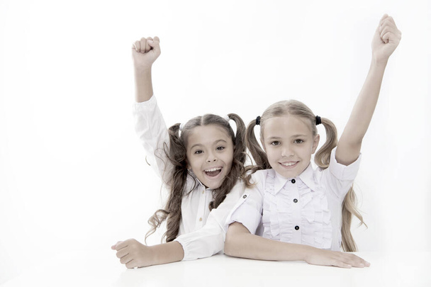 Schoolgirls happy keep hands up while sit at desk white background. Win school quiz. They know right answer. Schoolgirls emotional cheerful celebrate victory. Winners team. Teamwork and leadership - Photo, image