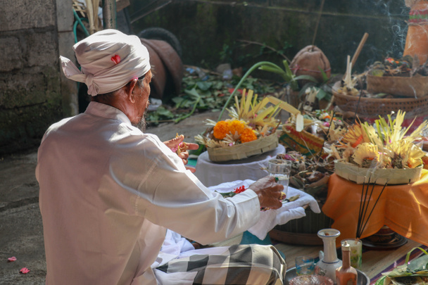 Πίσω όψη του Ινδουιστή ιερέα που προσεύχεται κατά τη διάρκεια τελετής γάμου. Pedanda κάθεται στο έδαφος μπροστά από τις προσφορές και εκτελεί γαμήλιες τελετές - Φωτογραφία, εικόνα