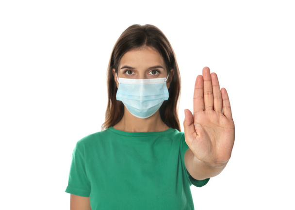 Woman in protective mask showing stop gesture on white background. Prevent spreading of coronavirus - Фото, зображення