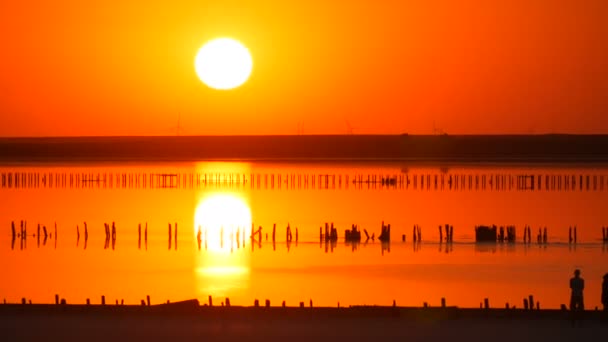 Incredibile incredibile tramonto rosso con un enorme sole rotondo su un lago salato sullo sfondo di sagome di mulini a vento - Filmati, video