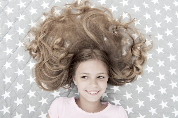 Child curly hairstyle relaxing. Conditioner mask organic oil keep hair shiny and healthy. Amazing hair tips. Keep hair curly even next morning. Girl child with long hair lay on bed top view - Foto, Imagen